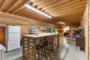Interior de madera con cocina, que incluye un refrigerador, una mesa de madera con sillas y una lámpara colgante.