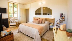 Een slaapkamer met een bed, een stoel, een bureau, een televisie en een boekenkast.