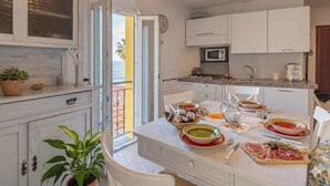 A compact kitchen with white cabinets, a microwave, and a dining area with a table set for two. - Holiday apartment with air conditioning (Imperia)