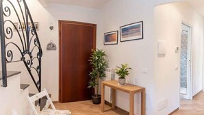 A hallway with a wooden door, a white chair, a small table with a plant, and two framed pictures on the wall. - Holiday apartment with air conditioning (Imperia)