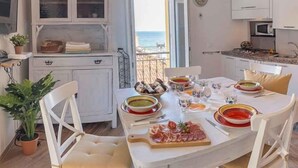 A dining area with a table set for four, a kitchen with white cabinets, and a view of the sea. - Holiday apartment with air conditioning (Imperia)