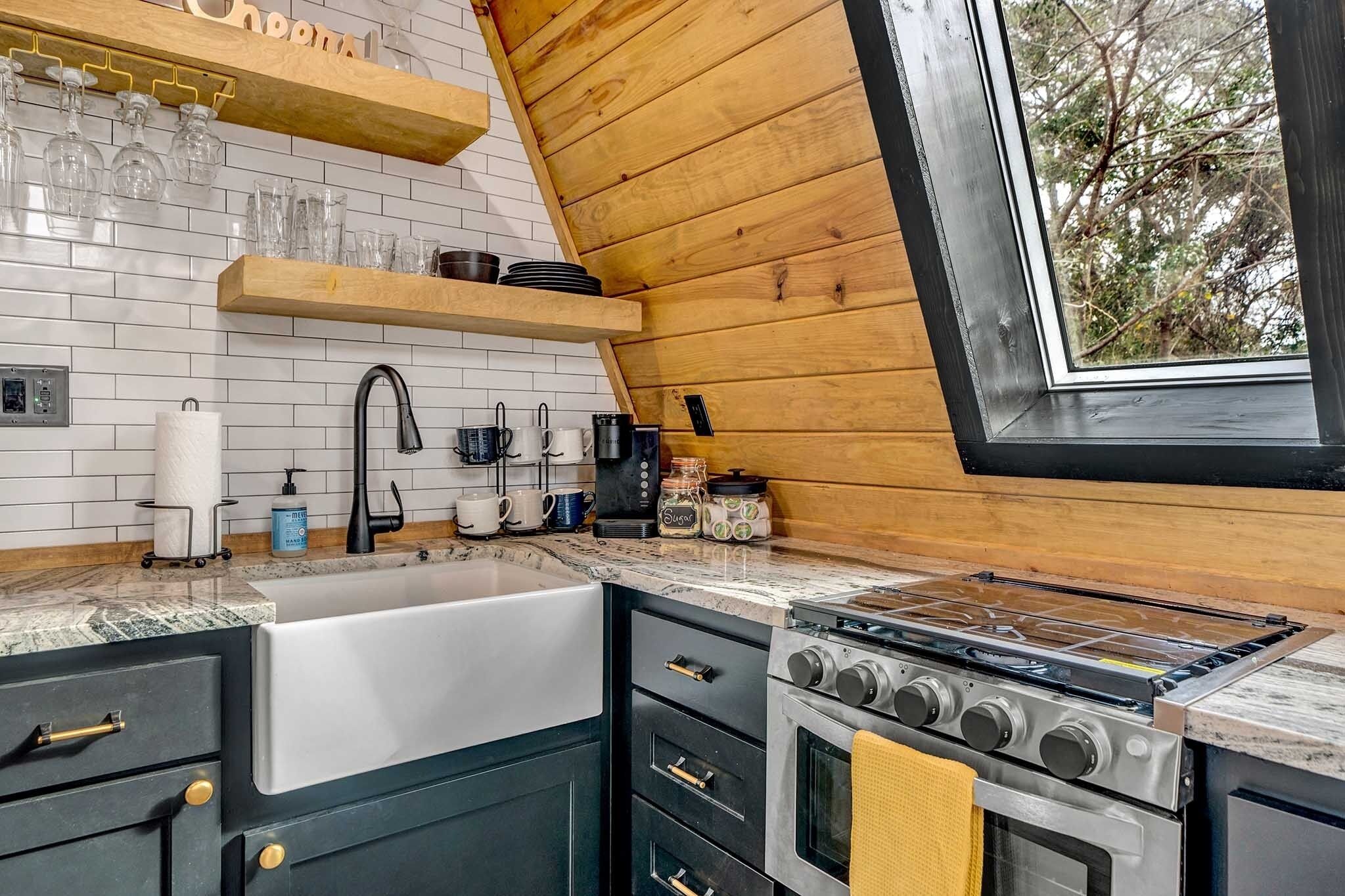A kitchen with a stove, sink, and wooden shelves.