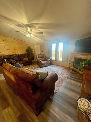 A living room with a brown leather sofa, a wooden accent wall, a ceiling fan, a fireplace, and a television. - Cast a line. Cruise the lake. Explore miles of nearby trails—or simply relax. (Warsaw)