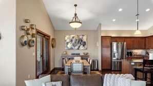 A modern kitchen with wooden cabinets, stainless steel appliances, and a dining area with a wooden table and chairs. - Riverfront Condo Steps to Downtown & Lake Michigan (Sheboygan)