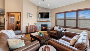 A living room with leather sofas, a coffee table, a fireplace, and a TV mounted on a brick wall. - Riverfront Condo Steps to Downtown & Lake Michigan (Sheboygan)