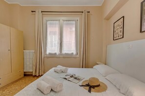 Ein Hotelzimmer mit Bett, Kleiderschrank, Heizkörper, einem Fenster mit Vorhängen und einer Wand mit gerahmten Bildern.