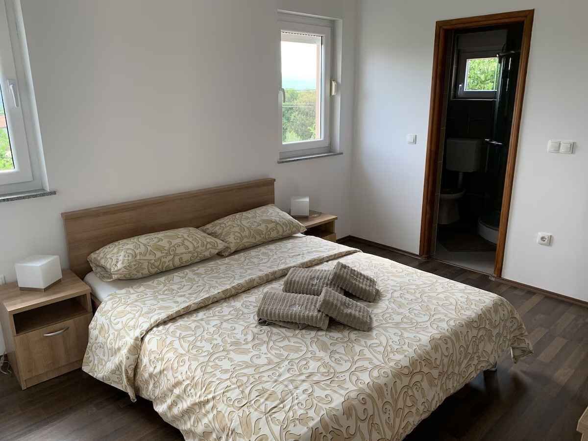 A bedroom with a bed, nightstands, a window, and a door leading to a bathroom.