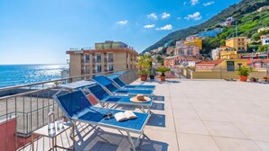 A rooftop terrace with sun loungers, a view of the sea, and buildings in the background. - Hotel Del Golfo 49, Laigueglia, Italy (Laigueglia)