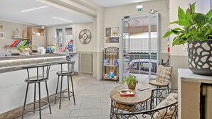 A modern kitchen with a marble countertop, bar stools, a dining area with a round table, and a view of the street through a glass door. - Hotel Del Golfo 71, Laigueglia, Italy (Laigueglia)