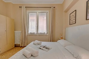 Ein Hotelzimmer mit Bett, Schrank, Heizkörper, Fenster mit Vorhängen und einer Wand mit gerahmten Bildern.