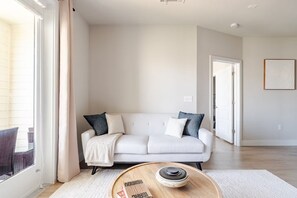 A modern living room with a white sofa, a round coffee table, and a view of the outside.