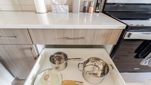 A kitchen with a countertop, a stove, and a drawer containing pots and a wooden spatula.