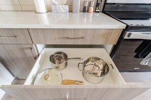 A kitchen with a countertop, a stove, and a drawer containing pots and a wooden spatula.