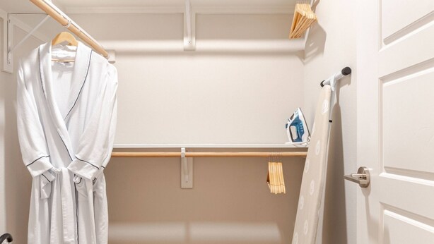 A small, well-lit room with a wooden floor, a white door, and a clothing rack with a robe.