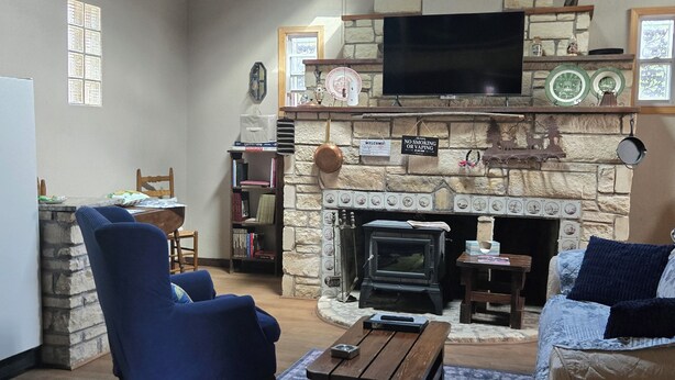 A living room with a stone fireplace, a television mounted above it, and a ceiling fan. - Historical, non Smoking, loft cottage with beautiful garden  near Riverwalk (Pueblo)