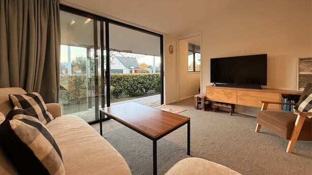 Un salon comprenant un canap é, une table basse, un téléviseur et une porte-fenêtre coulissante donnant sur un balcon.