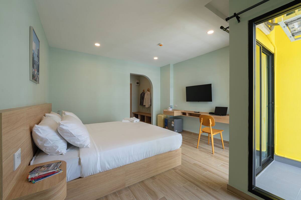 A modern hotel room with a bed, a desk, a chair, a TV, and a view through a large window.