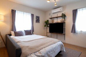 A bedroom with a bed, a TV, a shelf with decorative items, and an air conditioning unit. - Furano Ezo Murasaki B (Furano)