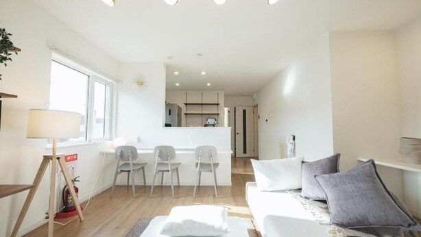 A modern living room with a sofa, chairs, a lamp, and a kitchen area in the background. - Furano Ezo Murasaki B (Furano)