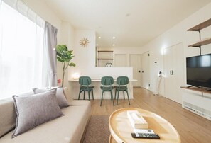 A modern living room with a sofa, a coffee table, a TV, and a dining area with chairs. - Furano Ezo Murasaki B (Furano)