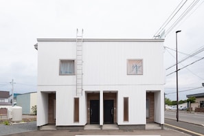 A modern two-story building with a white exterior, two black doors, and a small window on the upper floor. - Furano Ezo Murasaki B (Furano)