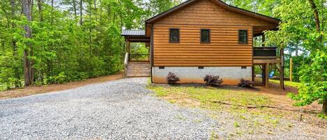 A wooden cabin with a porch, surrounded by trees.