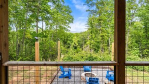Eine Holzterrasse mit Blick auf einen Wald. Blaue Stühle und eine Feuerstelle sind vorhanden.