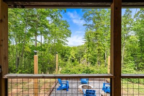 A wooden deck with a view of a forest. There are blue chairs and a fire pit. - Cozy Cabin with Great Views • Hot Tub • Wi-Fi (Murphy)