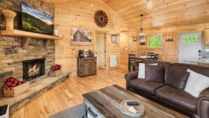 Ein gemütliches Blockhaus-Interieur mit Kamin aus Stein, Holzwänden, einer Ledersofa und einem Essbereich.