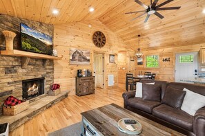 A cozy cabin interior with a stone fireplace, wooden walls, a leather sofa, and a dining area. - Cozy Cabin with Great Views • Hot Tub • Wi-Fi (Murphy)