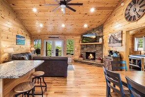 A wooden cabin interior with a stone fireplace, a large clock, and a cozy seating area. - Cozy Cabin with Great Views • Hot Tub • Wi-Fi (Murphy)