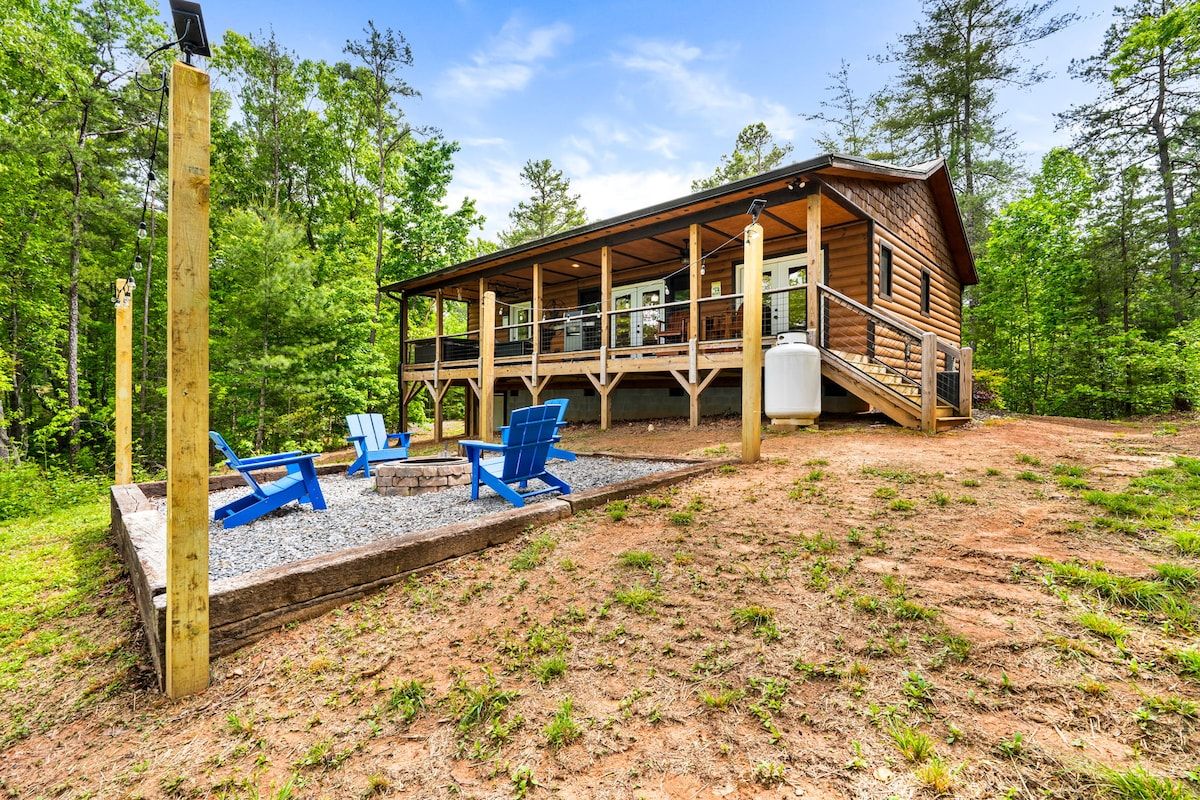 A cabin with a deck, surrounded by trees, and equipped with outdoor seating.