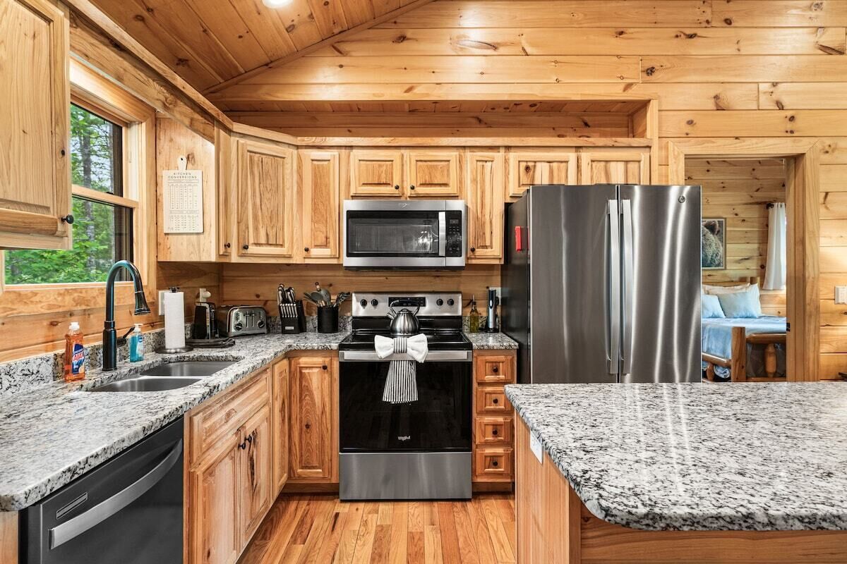 A kitchen with wooden cabinets, granite countertops, stainless steel appliances, and a view of the outdoors.
