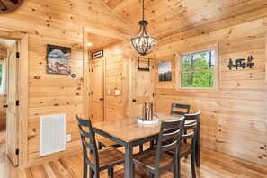 A wooden interior with a dining table and chairs, a chandelier, and a window with a forest view. - Cozy Cabin with Great Views • Hot Tub • Wi-Fi (Murphy)