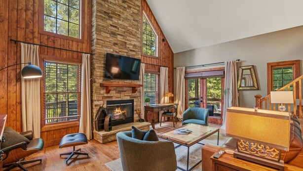 A spacious living room with a fireplace, wooden walls, large windows, and a television.