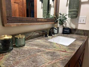 A bathroom with a marble countertop, a sink, a mirror, a towel rack, and a potted plant. - Lakeside Cabin minutes to Asheville (Buncombe County)
