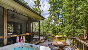A wooden deck with a hot tub, outdoor seating, and a view of a forest.