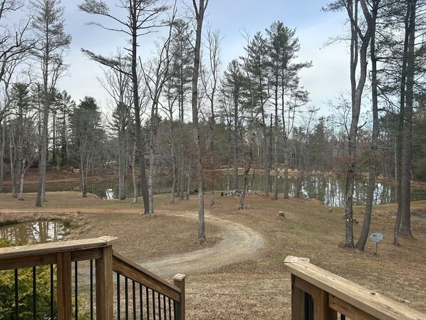 A wooded area with a dirt path leading to a pond, surrounded by trees and a wooden deck. - Lakeside Cabin minutes to Asheville (Buncombe County)