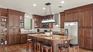 A kitchen with wooden cabinets, a central island with stools, a stainless steel refrigerator, and a pendant light. - Private Dock Waterfront Home in Miramar (Miramar Beach)