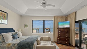 A bedroom with a bed, a sofa, a dresser, a TV, and a large window with a view of the beach. - Private Dock Waterfront Home in Miramar (Miramar Beach)
