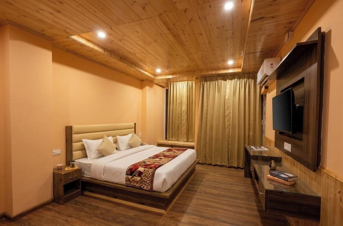 Una habitación de hotel con techo de madera, una cama con cabecera, un televisor montado en la pared y una ventana con cortinas.