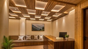Un área de recepción con un mostrador de madera, un banco con cojines, un cuadro enmarco con un paisaje y una planta en maceta.