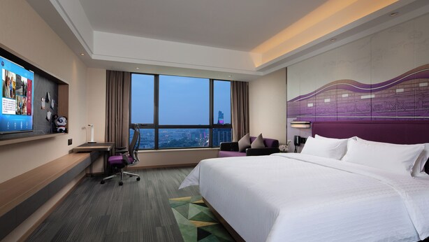A hotel room with a large bed, a desk with a chair, a TV, and a view of the cityscape. - Hampton by Hilton Hangzhou Xiaoshan People's Square (Hangzhou)