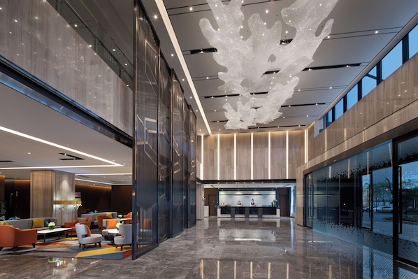 A modern lobby with a reception desk, seating area, and large windows.