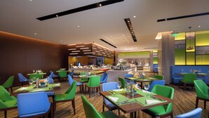 Un restaurant moderne avec des chaises vertes et bleues, des tables en bois et un coin bar.