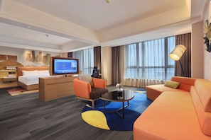 A hotel room with a bed, a TV, a sofa, a chair, a coffee table, and a large window.