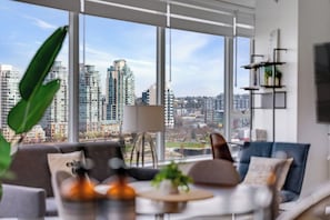 A modern living room with a large window, a sofa, a coffee table, and a bookshelf. - Cozy 2 Bedroom 2 Bathroom Downtown Vancouver/Pool/Hot Tub/Free Parking (Vancouver)