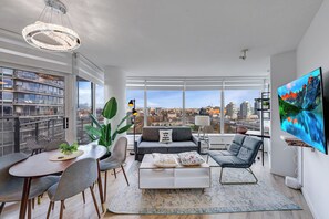 A modern living room with a dining area, large windows, and a city view. - Cozy 2 Bedroom 2 Bathroom Downtown Vancouver/Pool/Hot Tub/Free Parking (Vancouver)