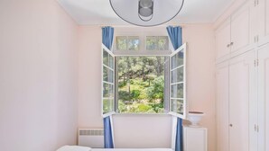 Ein Schlafzimmer mit großem Fenster, einem Bett, einem Nachttisch und einem Kleiderschrank.