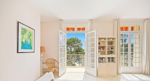 An open room with a view of the outdoors, a wicker chair, a bookshelf, and a framed picture on the wall. - Nouveau Le Rooftop - Clim chambres Et Piscine (HYERES)